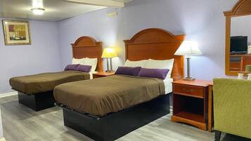 A hotel room with two beds, wooden headboards, bedside tables with lamps, a green chair, and a television on a cabinet.