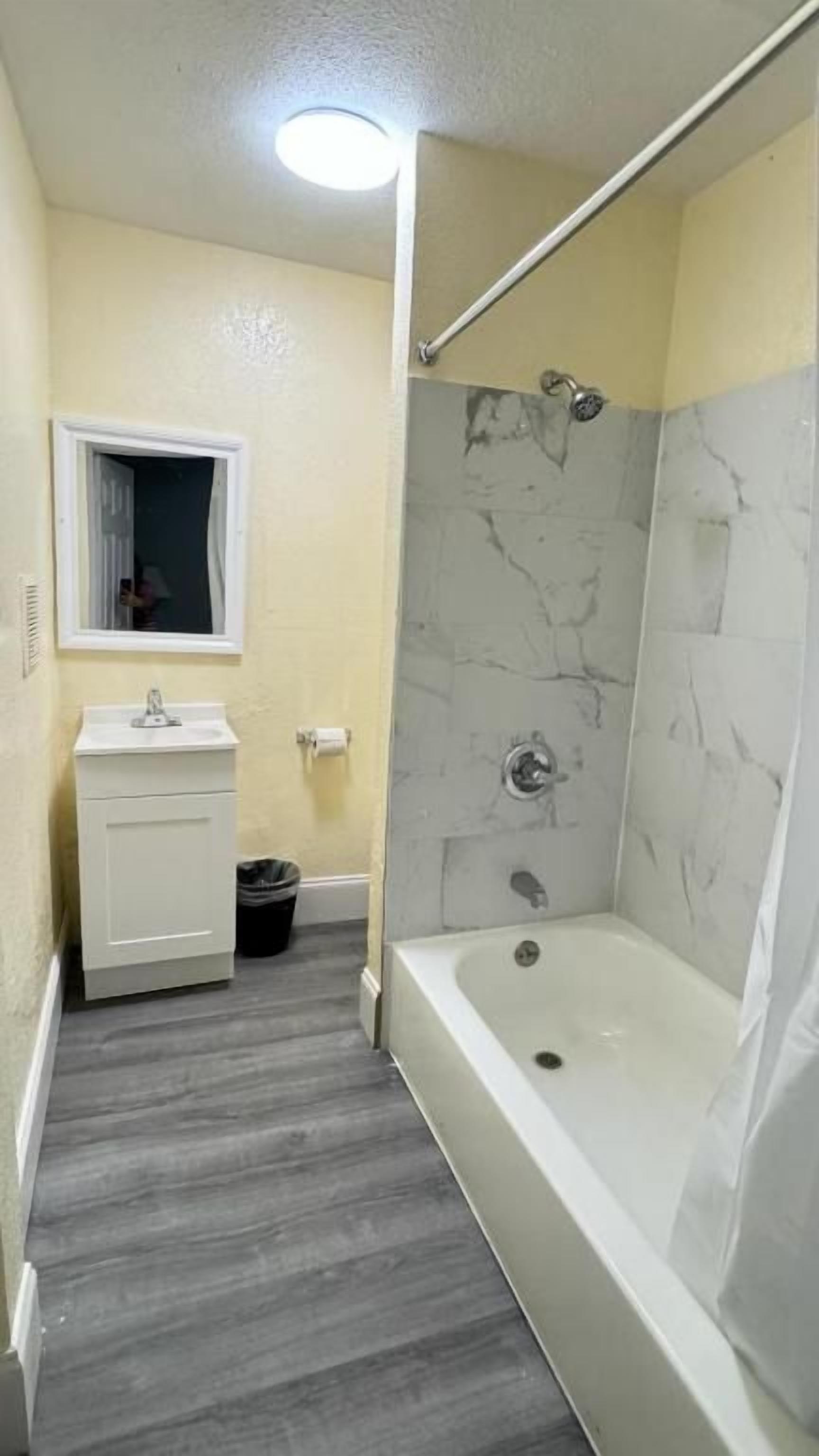 Une salle de bain avec une baignoire, une douche aux murs en marbre, un lavabo avec un miroir et une fenêtre.