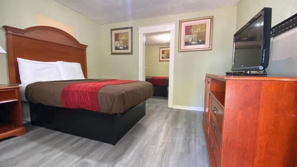 A hotel room with a bed, a television, a dresser, and framed pictures on the wall.
