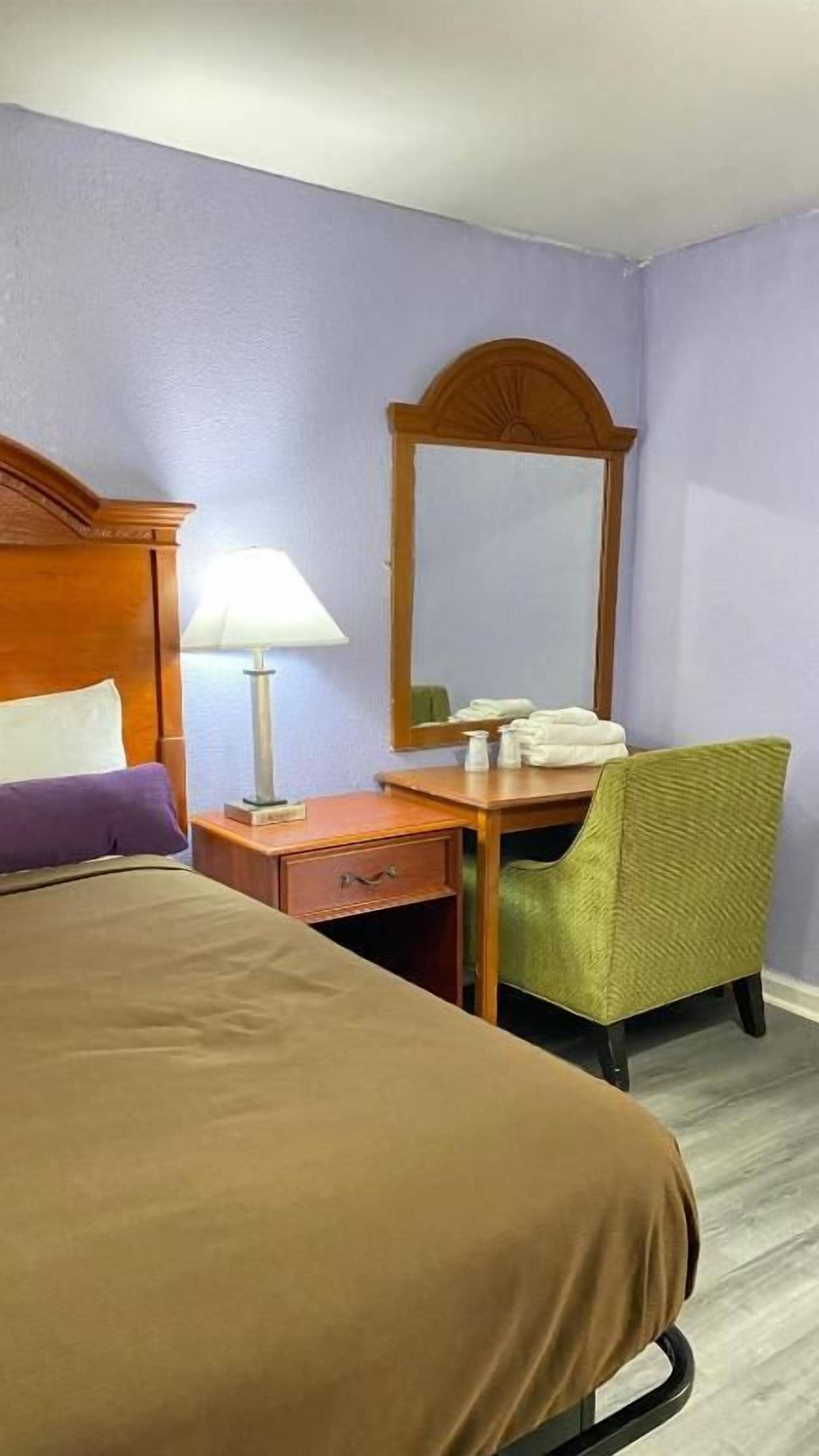 A hotel room with a bed, a desk, a chair, a lamp, and a mirror.