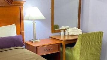 A hotel room with a bed, a desk, a chair, a lamp, and a mirror.