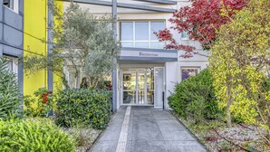 A modern building entrance with a 'Bienvenue' sign, surrounded by well-maintained greenery and a clear pathway.