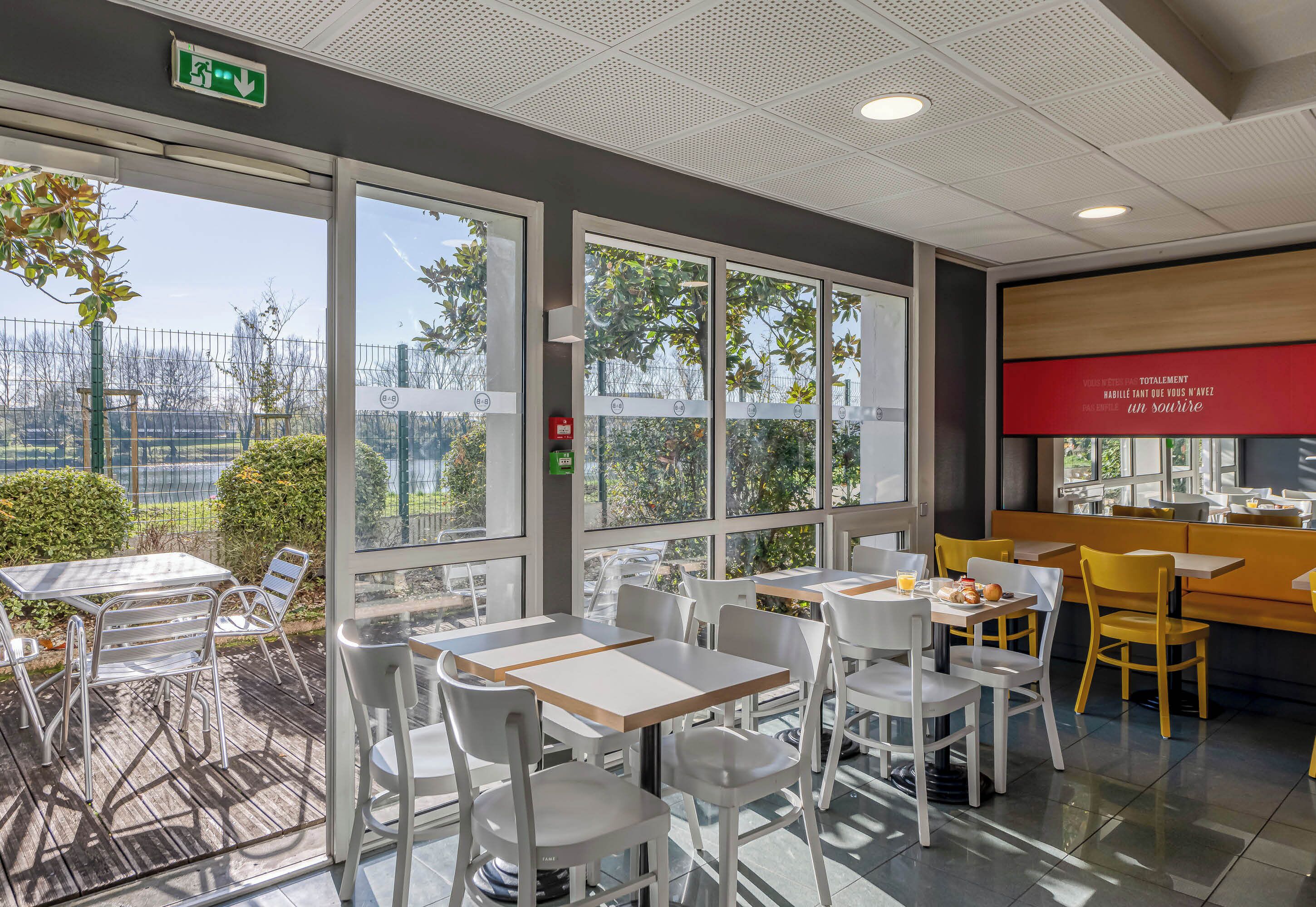 Un café moderne avec une terrasse, de grandes fenêtres et une enseigne rouge sur le mur.