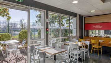 Un café moderne avec une terrasse, de grandes fenêtres et une enseigne rouge sur le mur.