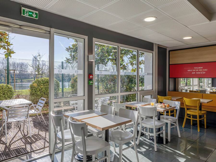 Een modern café met terras, grote ramen en een rood bord aan de muur.
