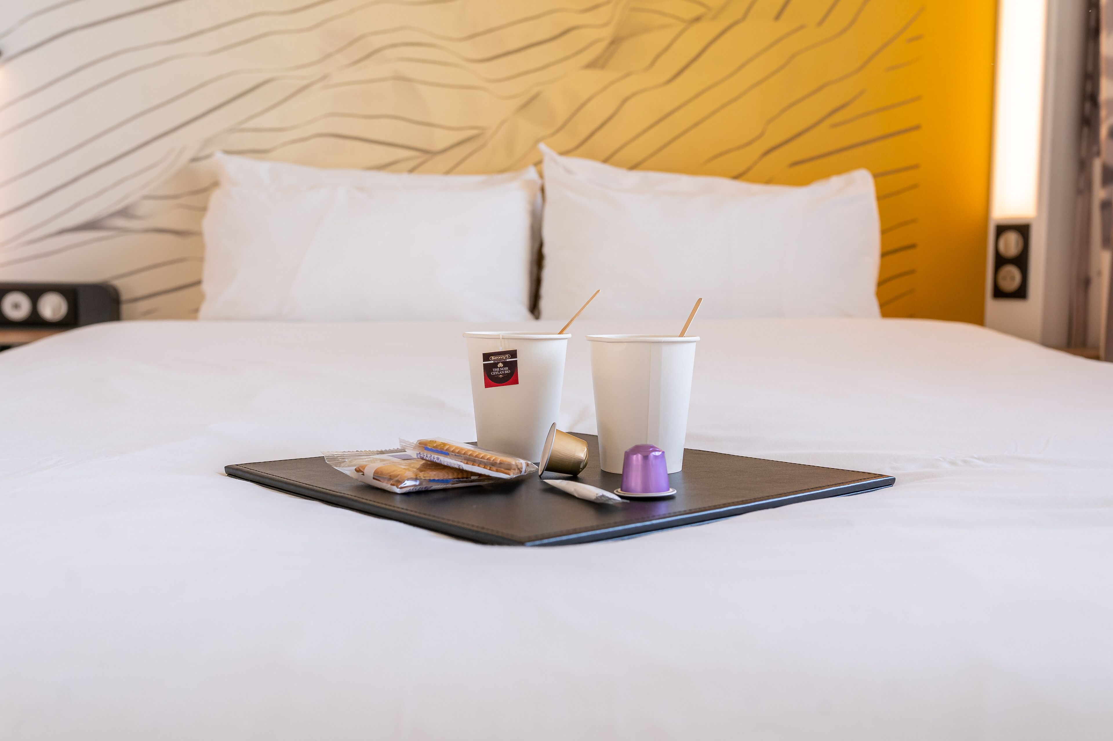 Una cama bien tendida con una bandeja de desayuno que incluye dos tazas, un muffin y un recipiente pequeño.