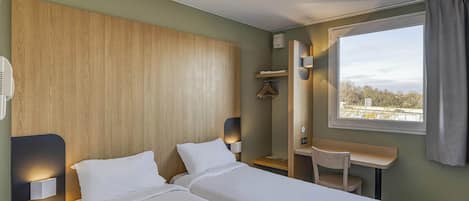 A hotel room with two beds, a desk, a chair, a window with a view, and a wooden headboard.