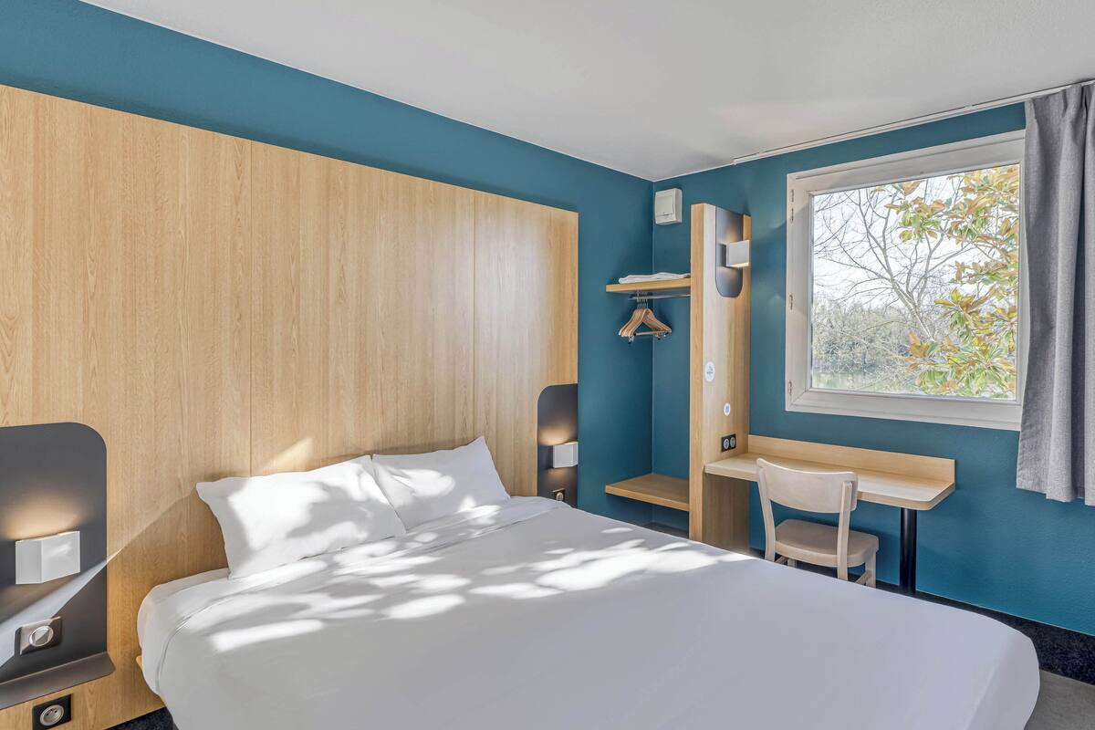 Une chambre d’hôtel moderne avec un grand lit, un bureau et une fenêtre donnant sur la verdure.