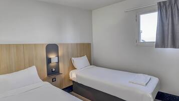 A hotel room with two beds, a bedside table with a lamp, a window with curtains, and a view of the sky.