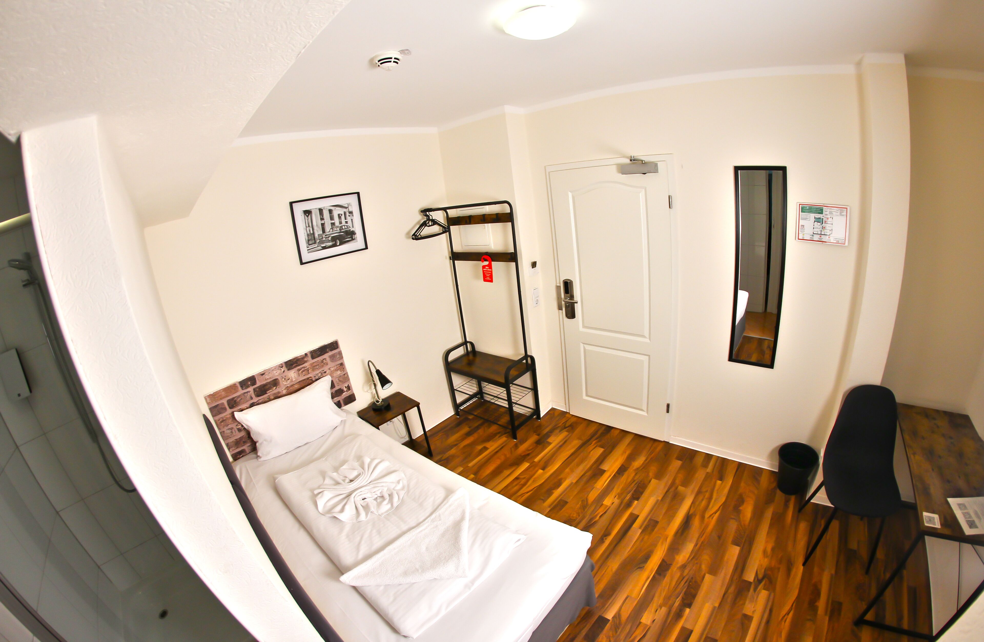 A hotel room with a bed, a desk, a chair, a mirror, and a door.