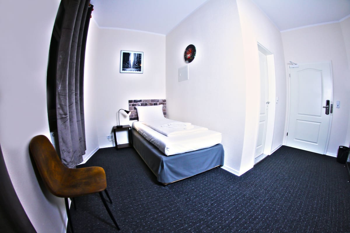A hotel room with a bed, a chair, a picture on the wall, and a door.