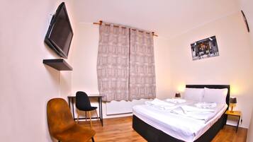 Une chambre à coucher comprenant un lit, une chaise, un bureau, un téléviseur et une fenêtre avec des rideaux.