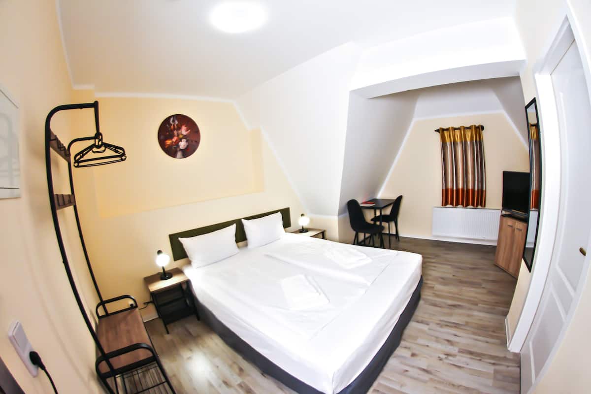 A hotel room with a large bed, a desk, a chair, a TV, and a clock on the wall.