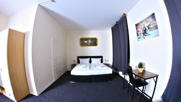 Habitación de hotel con cama, escritorio, silla, un cuadro en la pared y una puerta.