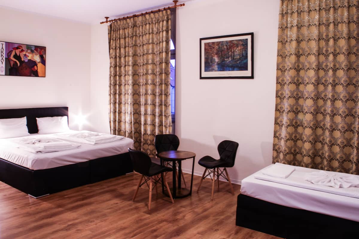 A hotel room with two beds, a small round table, two chairs, and a painting on the wall.