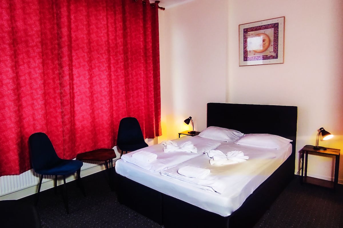 A hotel room with a bed, two chairs, a small table, and two bedside lamps.