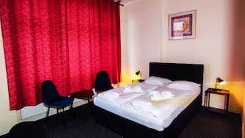 Una habitación de hotel con una cama, dos sillones, una mesita y dos lámparas de noche.