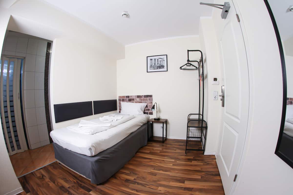A modern bedroom with a bed, a nightstand, a wall-mounted shelf, and a door.