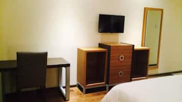Una camera d'albergo con una scrivania in legno, una sedia, una TV a parete e un letto con biancheria bianca.