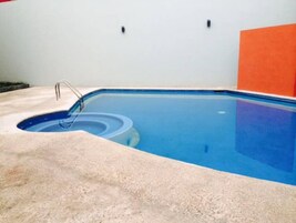 Una piscina rectangular con superficie de agua azul cristalina, una escalera metálica y un borde de hormigón.