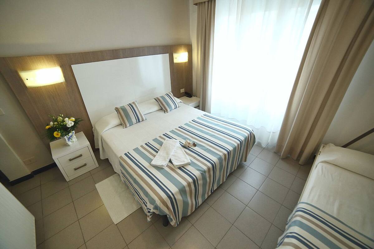 A hotel room with a large bed, a bedside table with a vase of flowers, and a nightstand.