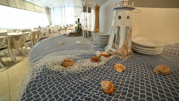A dining area with a blue patterned tablecloth, white chairs, and a stack of plates. - Hotel Villa Rosa (Sestri Levante)