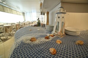 Un comedor con mantel azul estampado, sillas blancas y una pila de platos.