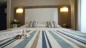 A hotel room with a large bed, striped bedding, two pillows, a bedside table with a lamp, and a vase with flowers. - Hotel Villa Rosa (Sestri Levante)