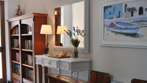 A room with a wooden bench, a white console table with lamps, a bookshelf, and a painting on the wall. - Hotel Villa Rosa (Sestri Levante)