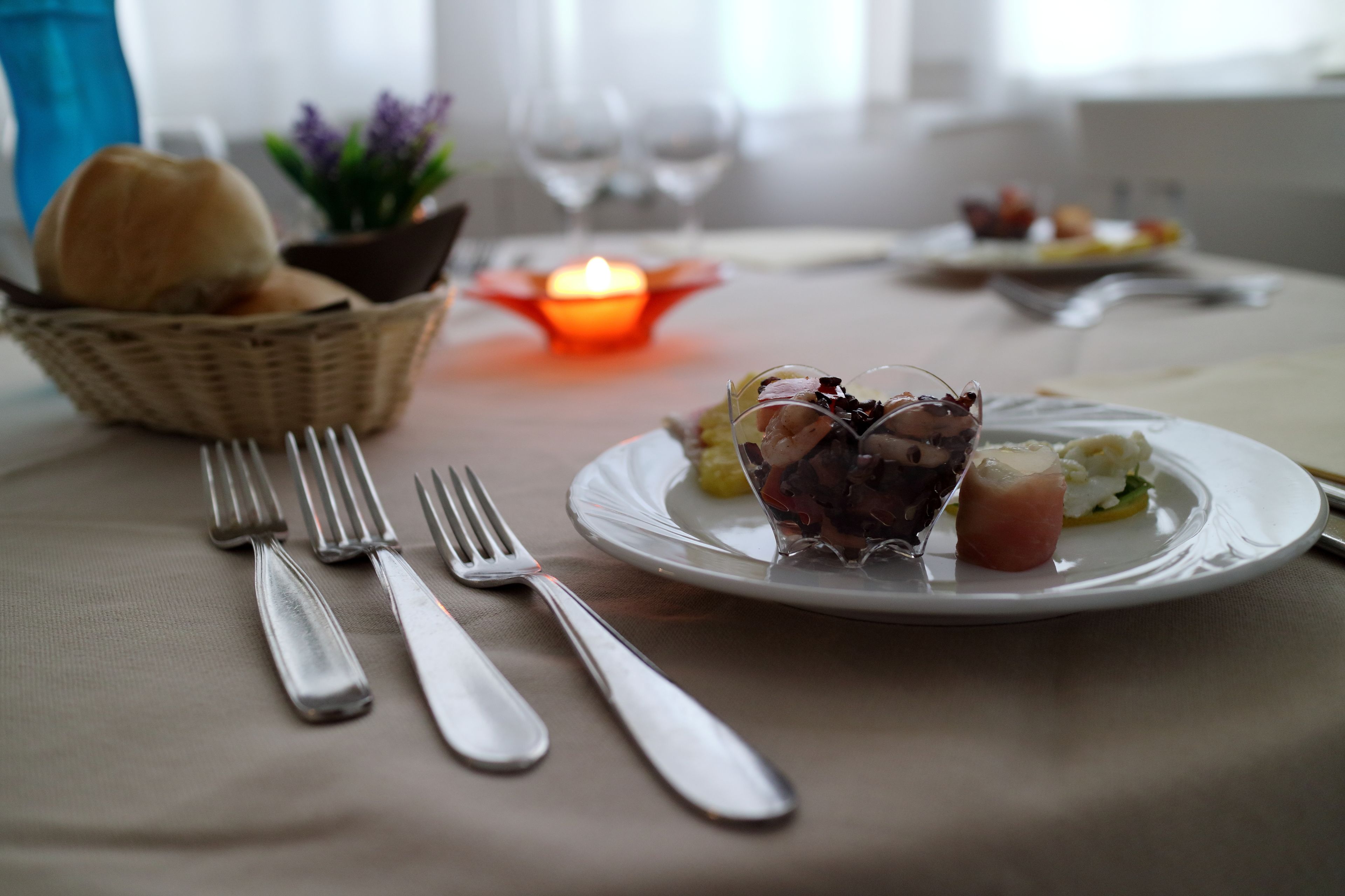 Un tavolo da pranzo con un piatto di cibo, un cestino di pane e una candela accesa.