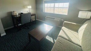 A hotel room with a desk, chair, sofa, and a large window providing a view of the outdoors.