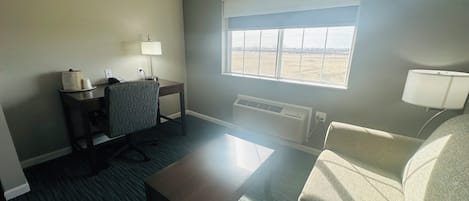 A hotel room with a desk, chair, sofa, and a large window providing a view of the outdoors.