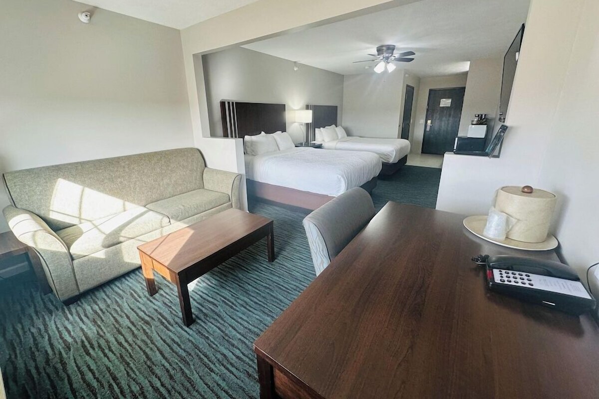 A hotel room with a sofa, a bed, a desk, a chair, a lamp, and a ceiling fan.