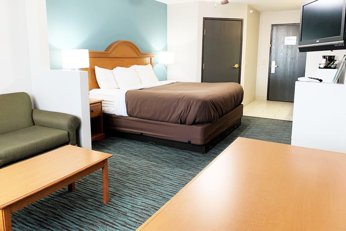 A hotel room with a bed, a desk, a chair, a television, and a door.