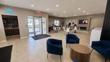 A modern interior with a reception area, seating, and a kitchen visible through the glass doors.