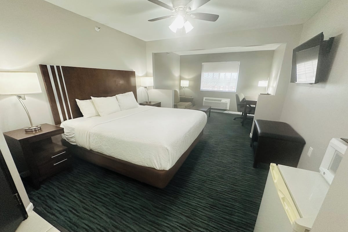 A hotel room with a large bed, a desk, a chair, a lamp, a ceiling fan, and a window.