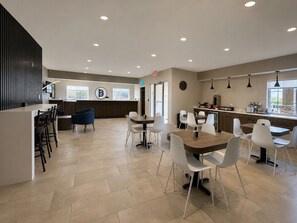 A modern dining area with a central island, white chairs, and a kitchen in the background. - BridgePointe Inn & Suites by BPhotels, Lincoln I-80/27th St (Lincoln)