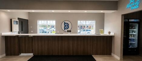 A reception desk with a logo, a neon sign, and a view of parked cars outside.