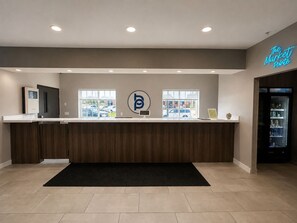 A reception desk with a logo, a neon sign, and a view of parked cars outside. - BridgePointe Inn & Suites by BPhotels, Lincoln I-80/27th St (Lincoln)