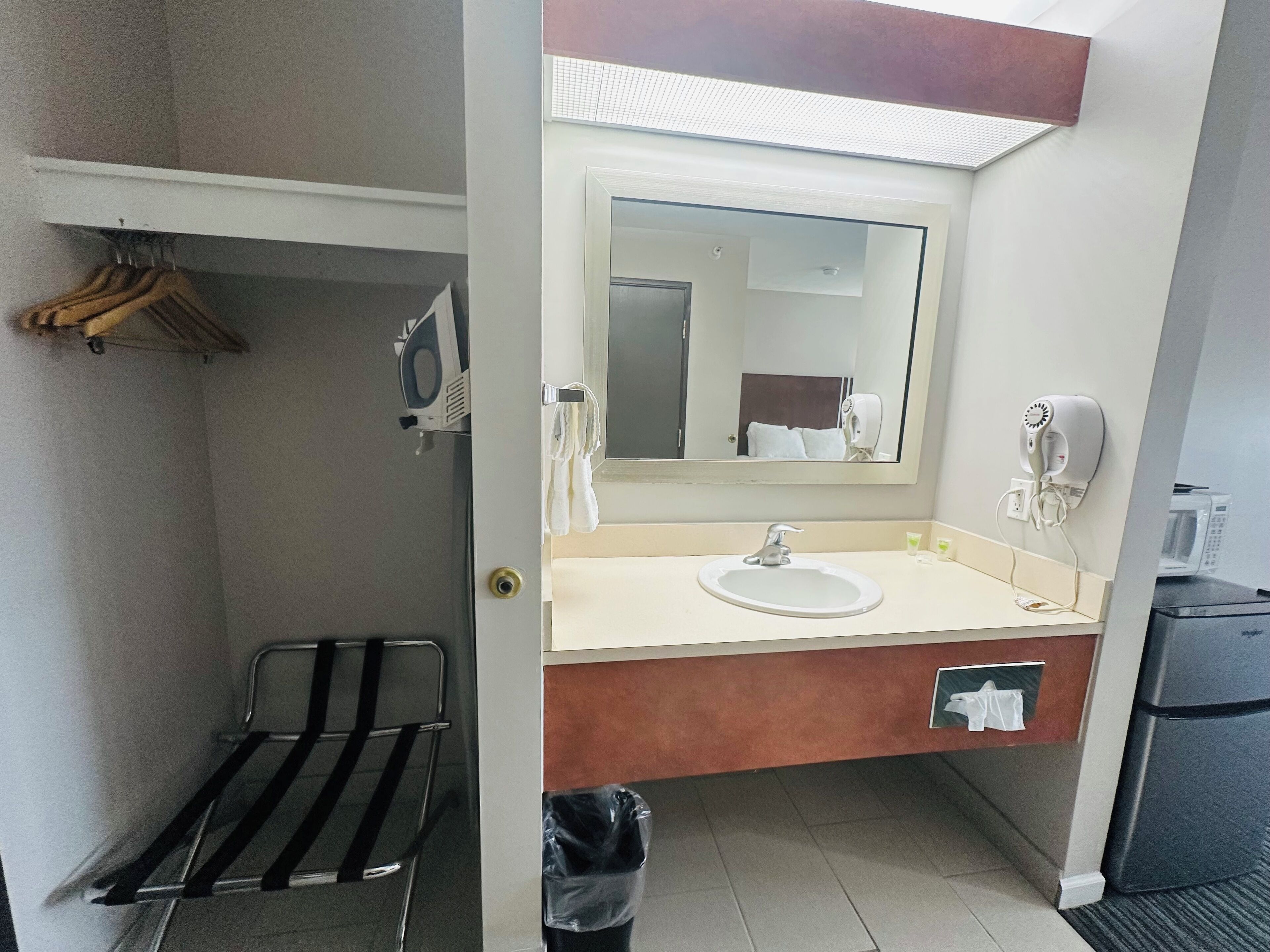 Un baño de hotel con lavamanos, espejo, toallero y una silla negra.