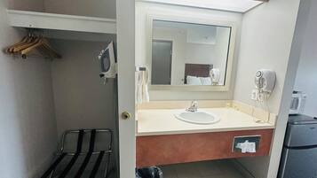 Un baño de hotel con lavamanos, espejo, toallero y una silla negra.
