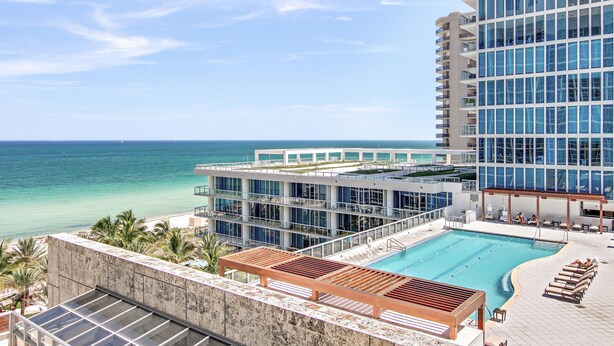 A rooftop pool with lounge chairs, a clear view of the ocean, and a modern building with balconies. - Carillon Miami Wellness Resort (Miami Beach)