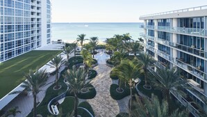 A modern hotel with a central courtyard featuring palm trees and a pathway leading to the beach. - Carillon Miami Wellness Resort (Miami Beach)