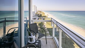 A balcony with a view of the beach and ocean, a chair, a bottle of champagne, and a glass. - Carillon Miami Wellness Resort (Miami Beach)
