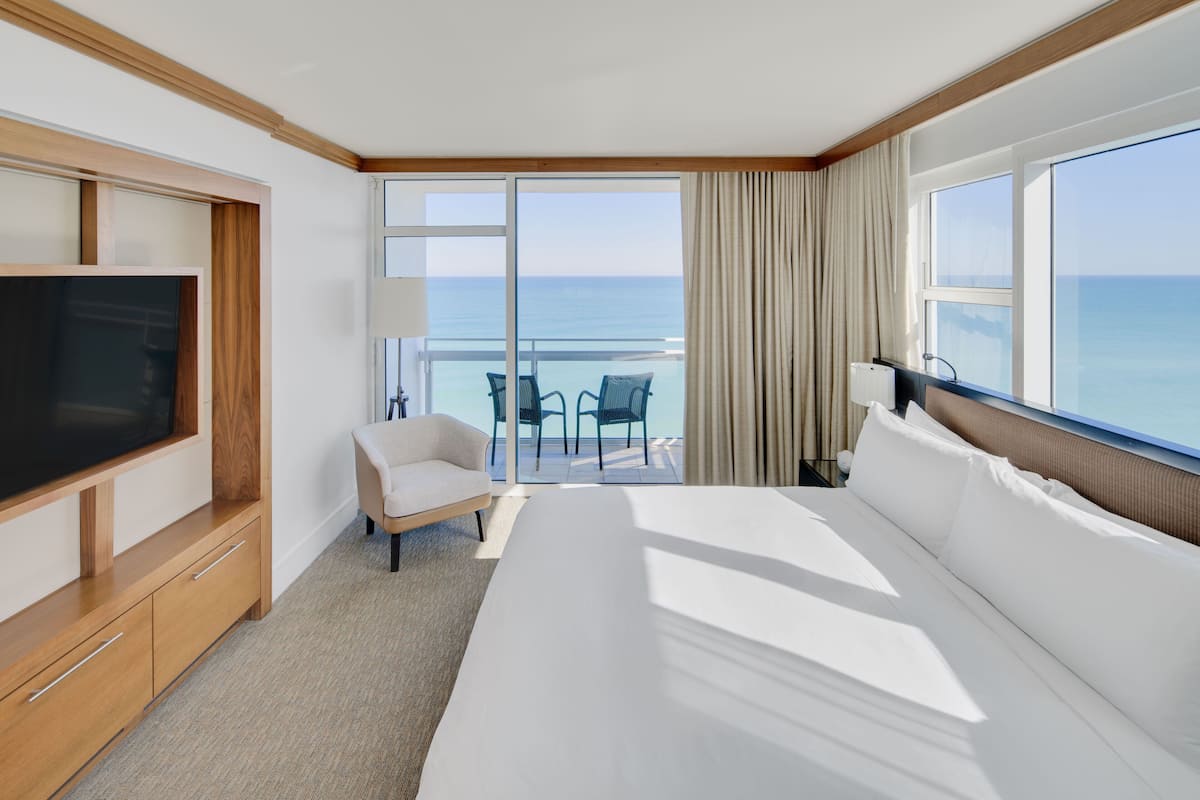 A hotel room with a large bed, a TV, a sofa, and a balcony with a view of the sea.