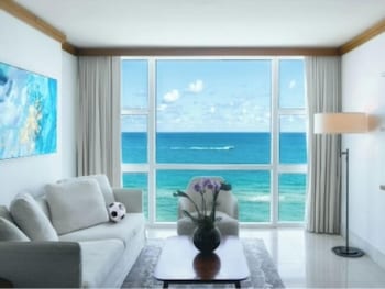A hotel room with a large bed, a TV, a chair, and a view of the ocean. at Carillon Miami Wellness Resort
