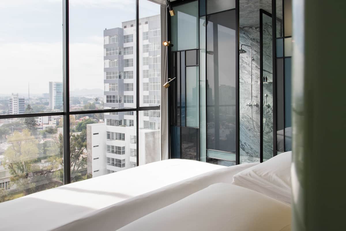A modern bedroom with a large window, a bed, and a shower area.