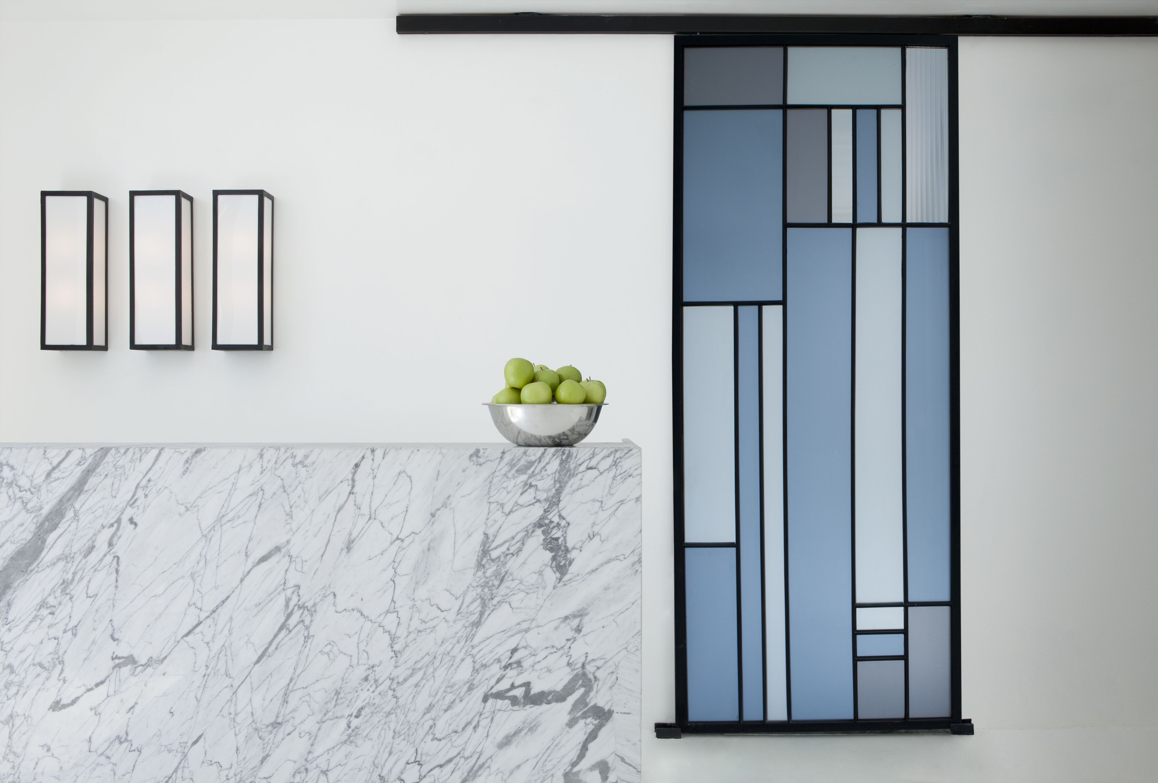 Uma cozinha moderna com bancada de mármore, uma tigela de maçãs verdes e um painel decorativo na parede.