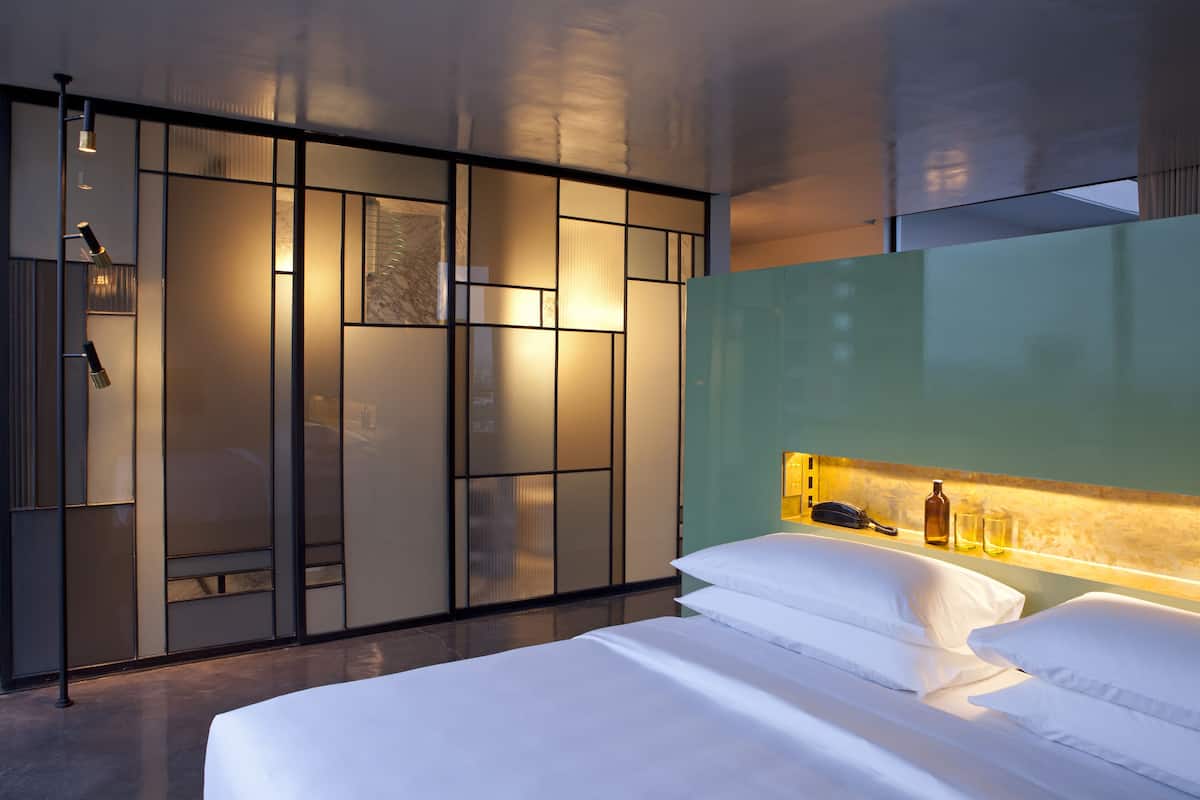 A modern hotel room with a large bed, a nightstand with a lamp, and a sliding door closet.