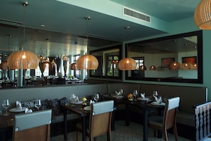 Um restaurante com várias mesas, cadeiras e luminárias pendentes.